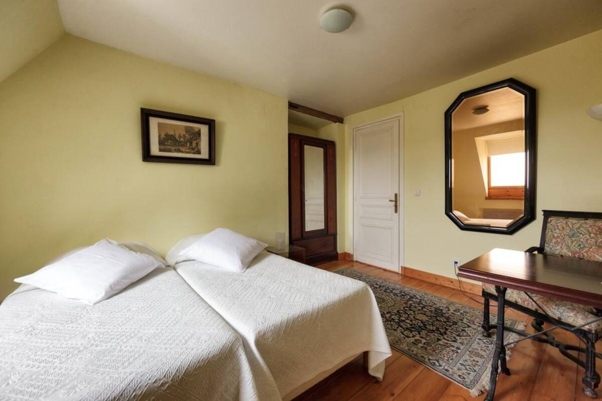 A bedroom with two beds, a wooden table, a mirror, and a door.