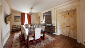 A dining room with a wooden table, chairs, a chandelier, and a red carpet. - Château du Jard (Chaumont-en-Vexin)