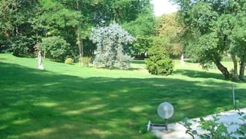 A well-maintained grassy area with a spherical sculpture, surrounded by trees and a statue in the background.
