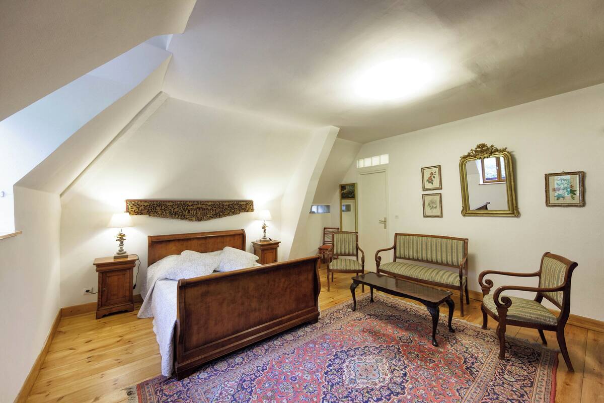A bedroom with a wooden bed, a sitting area with a sofa and chairs, a patterned rug, and a large mirror on the wall.