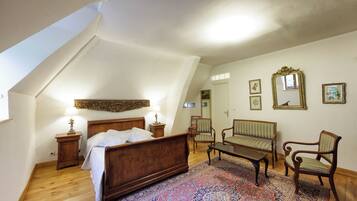 Un dormitorio con cama de madera, una zona de estar con sofá y sillones, un tapete estampado y un espejo grande en la pared.