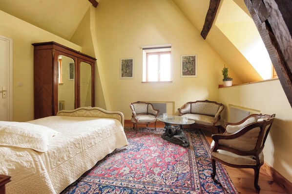 Un dormitorio con una cama grande, dos sillones, una mesita, un espejo y una ventana.