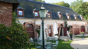 A courtyard with outdoor seating, a brick building with multiple windows and doors, and a lamp post. - Château du Jard (Chaumont-en-Vexin)