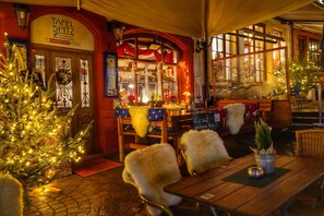 A cozy outdoor seating area with wooden tables and chairs, a Christmas tree, and a sign for Tafel Spitz Restaurant. - Marktplatzhotel - Restaurant Tafelspitz (Weinheim)