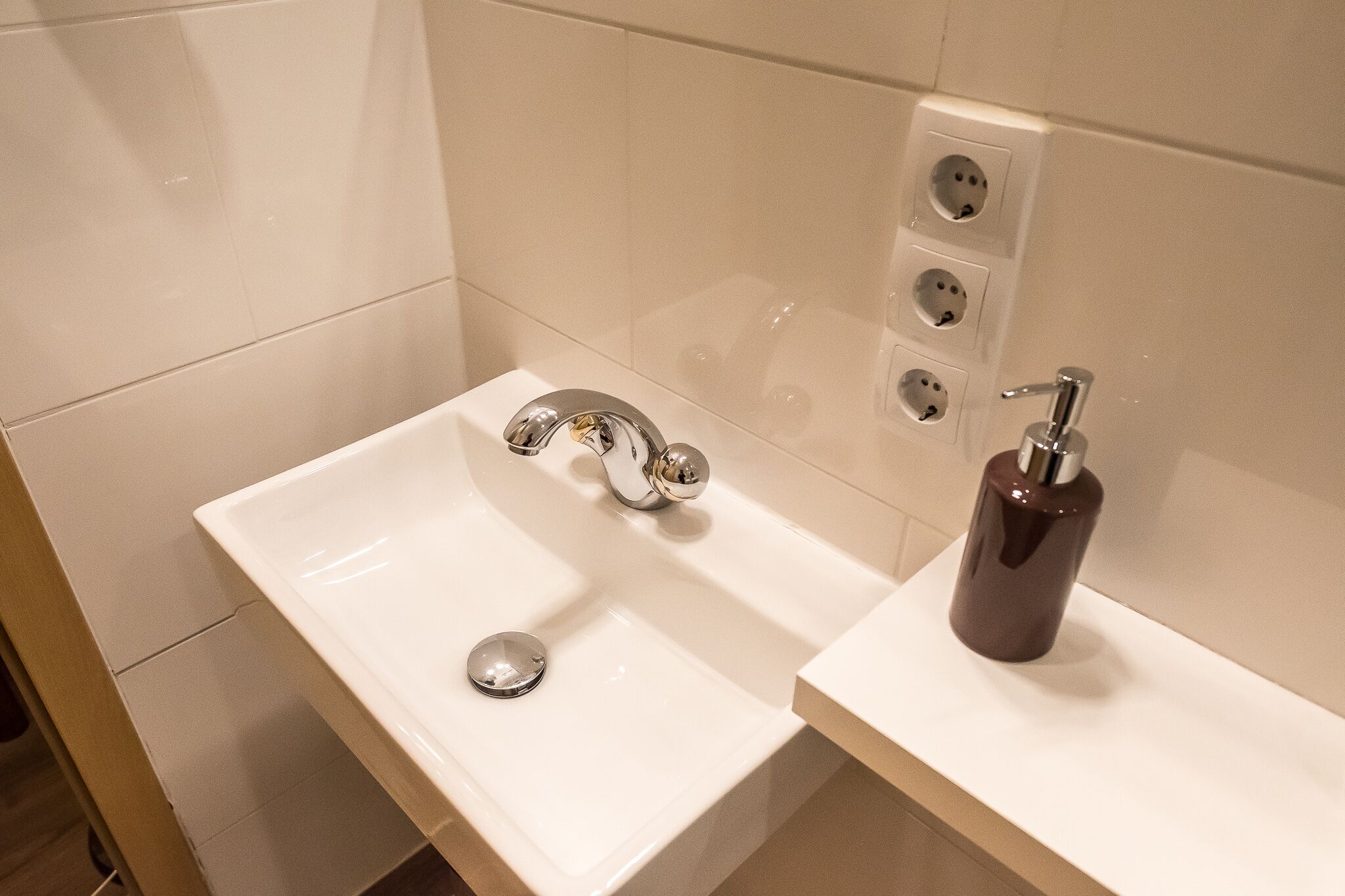 A bathroom with a white sink, a chrome faucet, and a dark-colored soap dispenser.