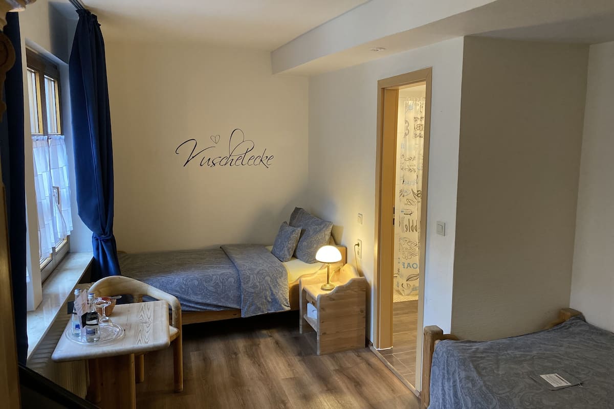 A small, cozy bedroom with two beds, a desk with a lamp, and a window with curtains.