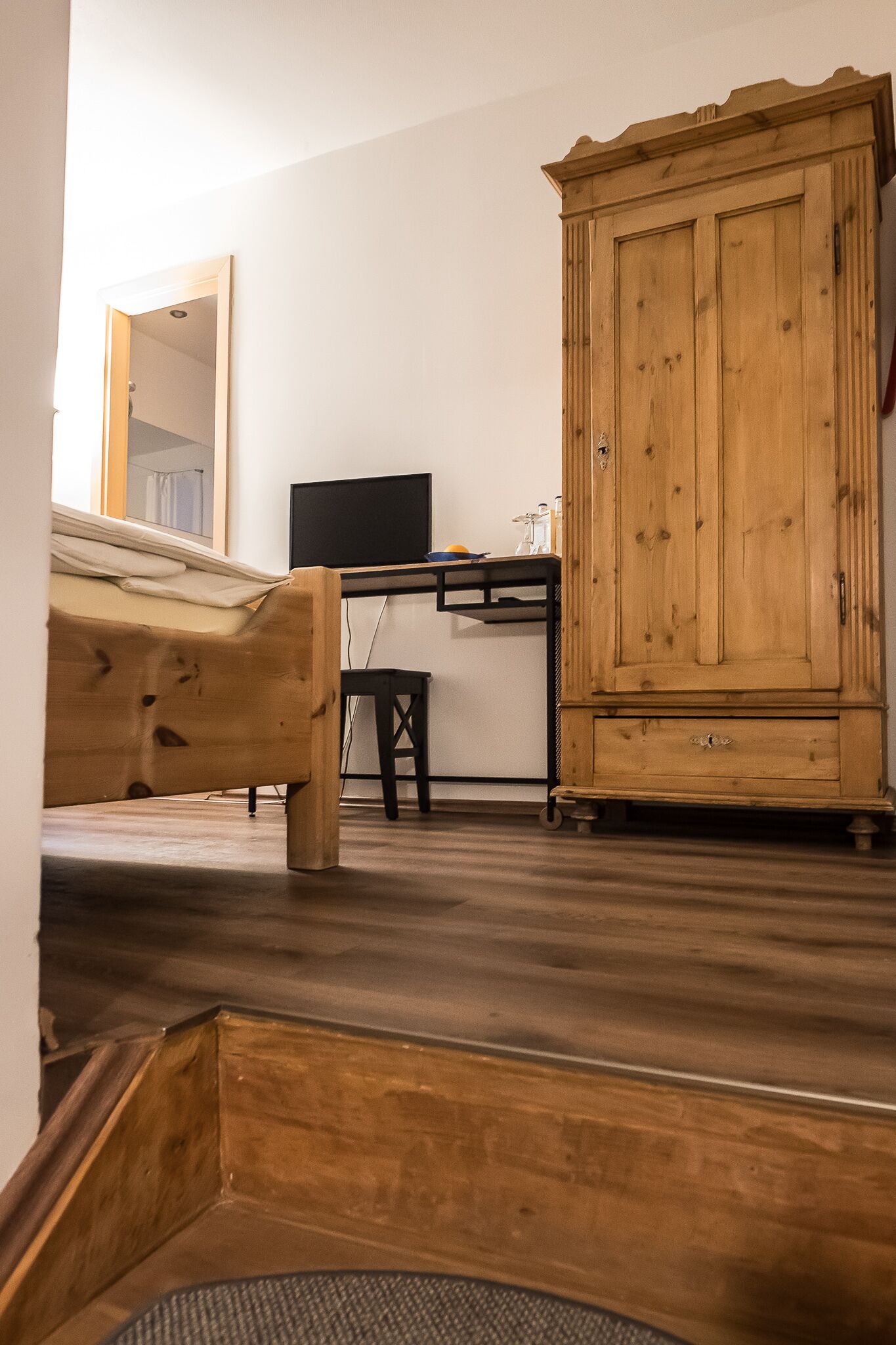Una habitación con una cama de madera, un escritorio con una computadora y un armario de madera.