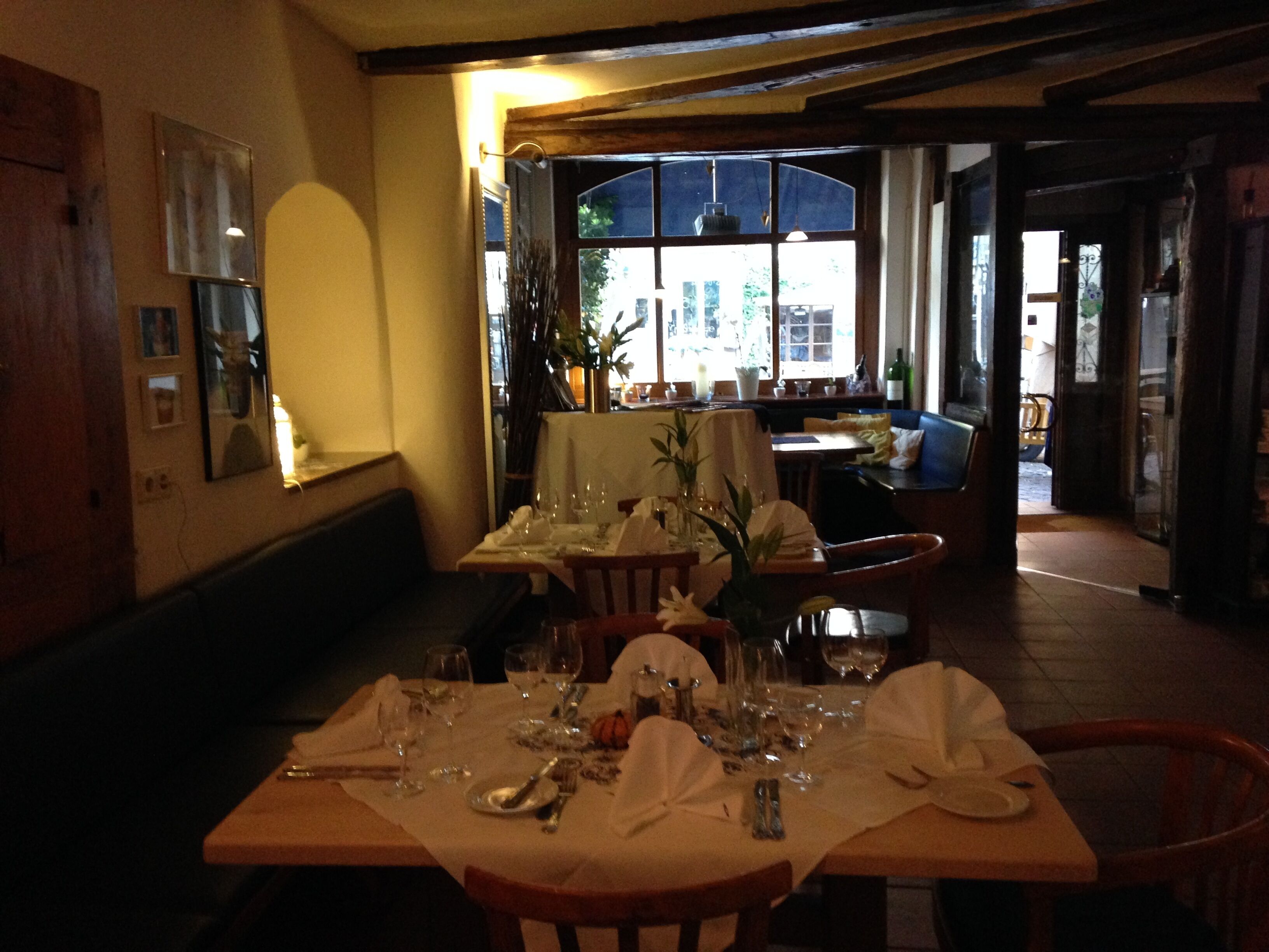 A restaurant with a wooden table set for dining, a bench, and a view of the street through a window.
