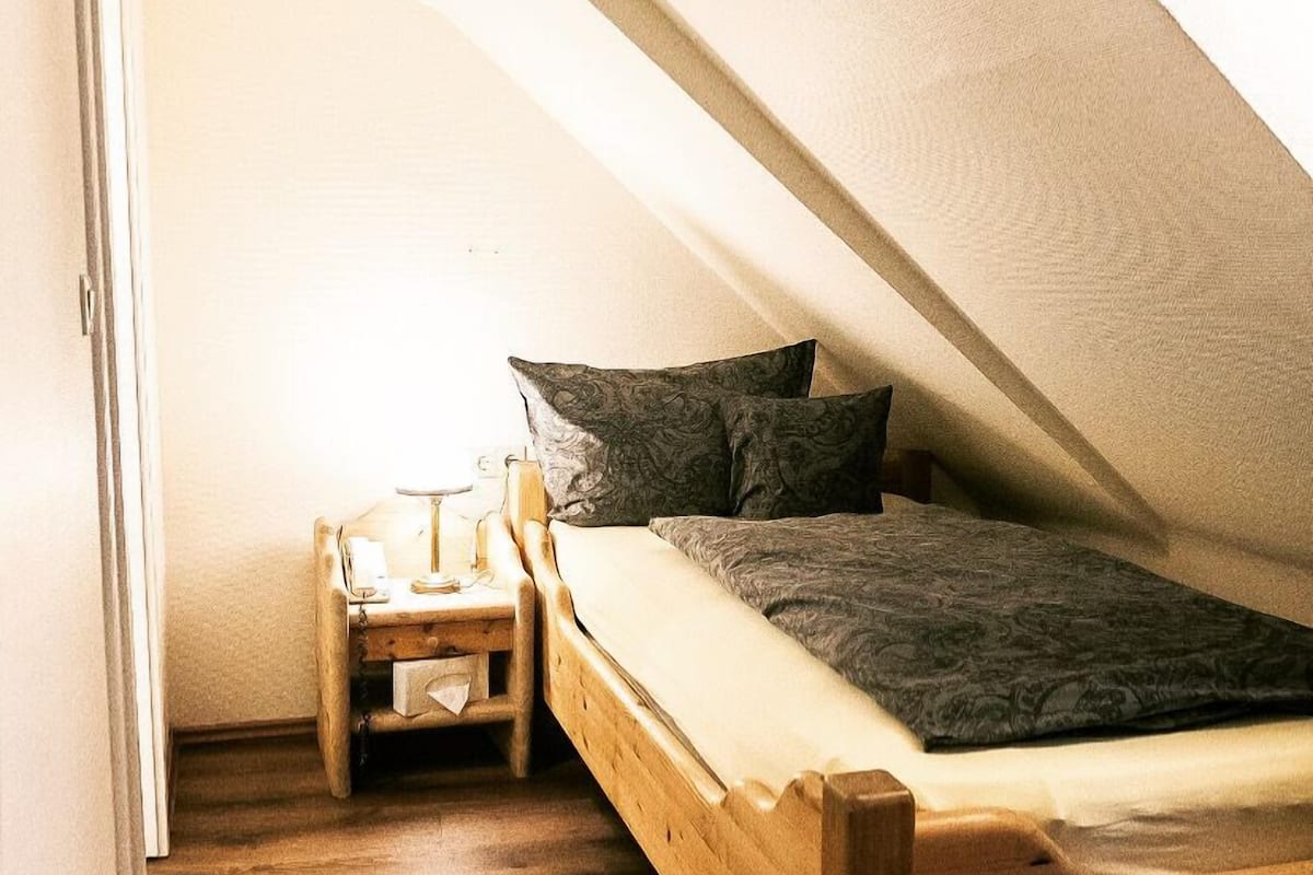 A small, cozy attic bedroom with a wooden bed, a nightstand, and a lamp.