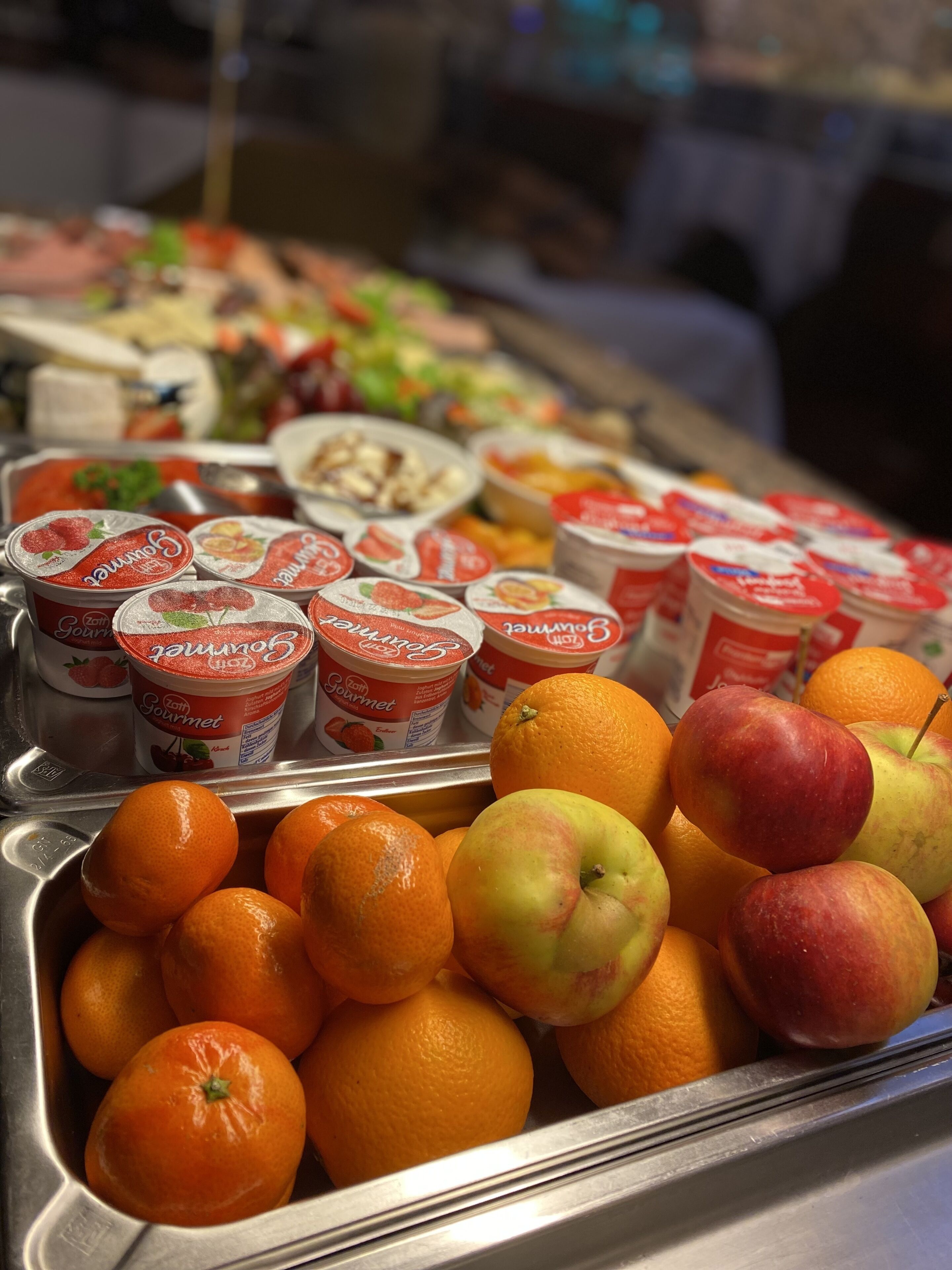Een presentatie van yoghurtbekers en verse vruchten, zoals appels en sinaasappels.