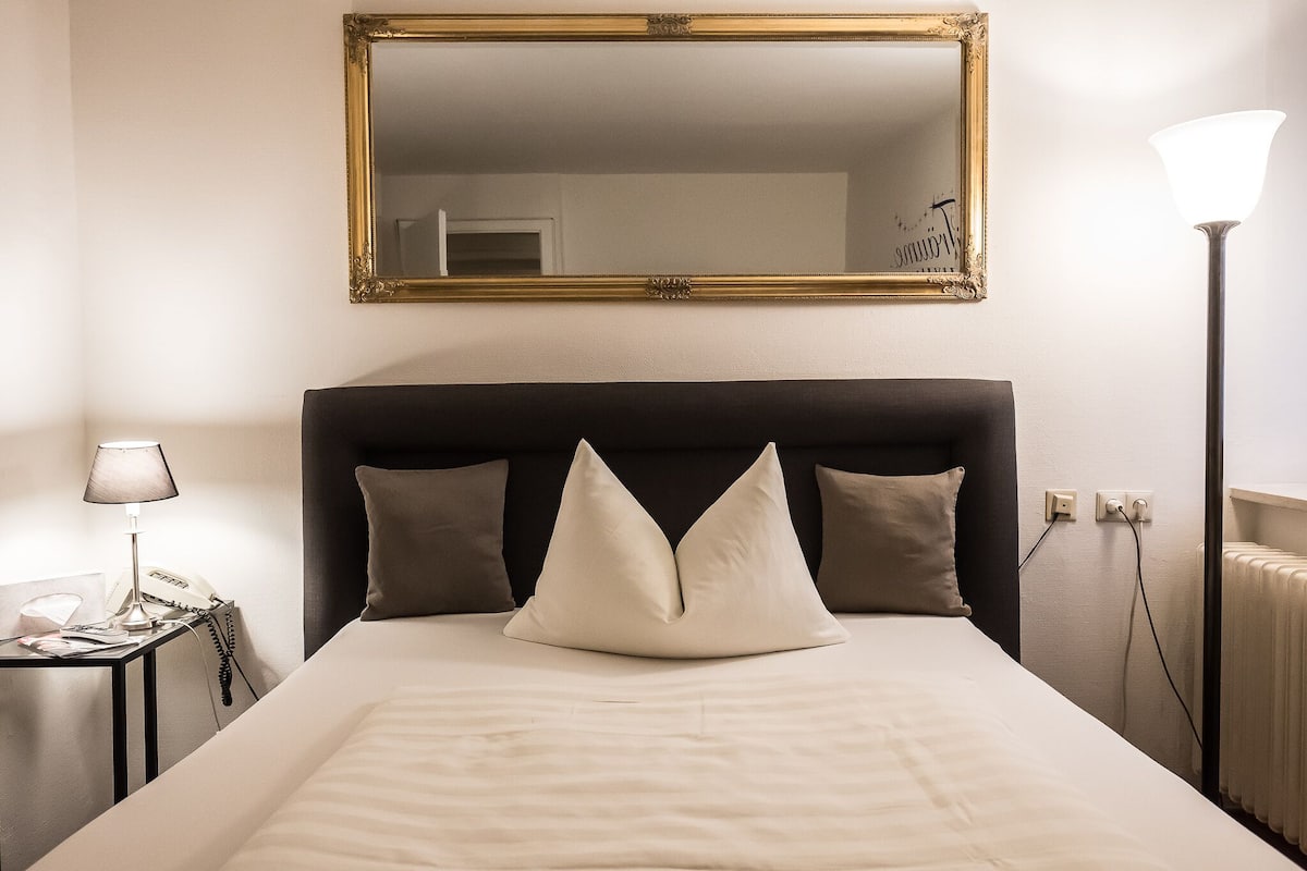 A neatly made bed with a black headboard, two bedside lamps, and a large mirror above the bed.