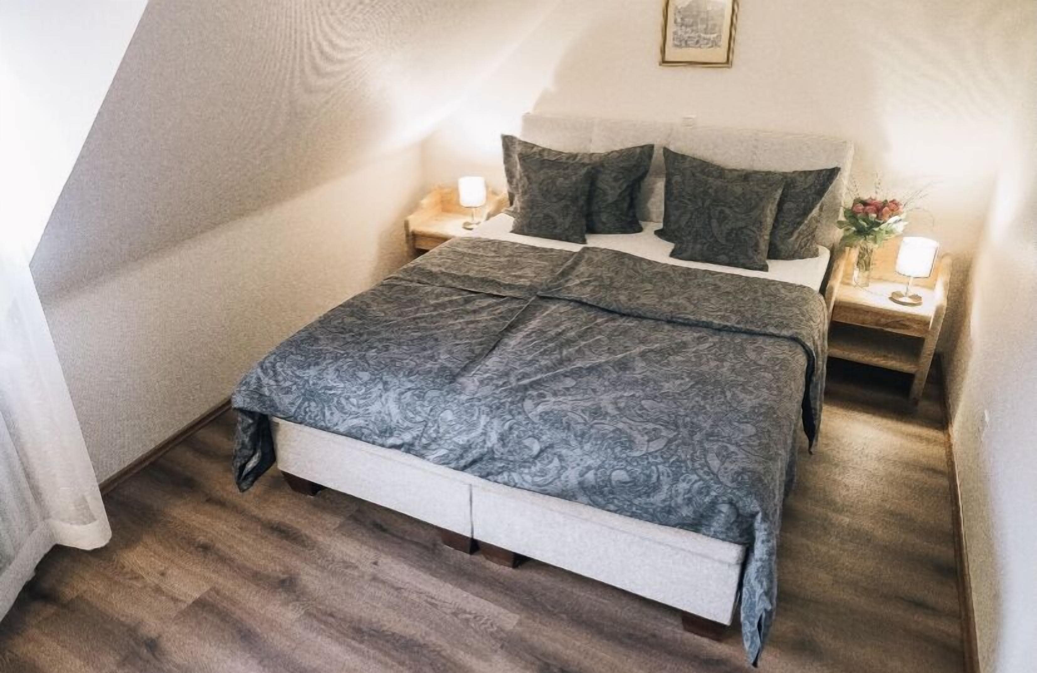 A bedroom with a bed, two bedside tables, and a nightstand with a lamp.