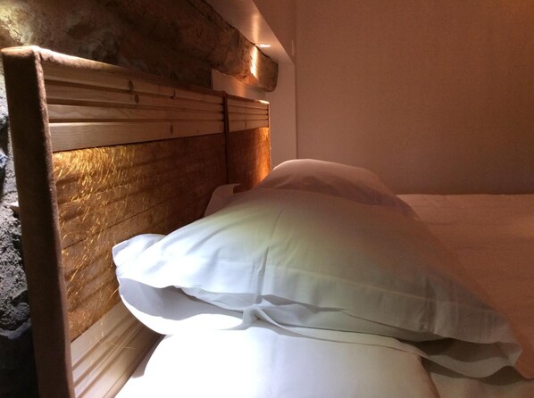 A bed with white bedding in a room with wooden headboard and a stone wall.