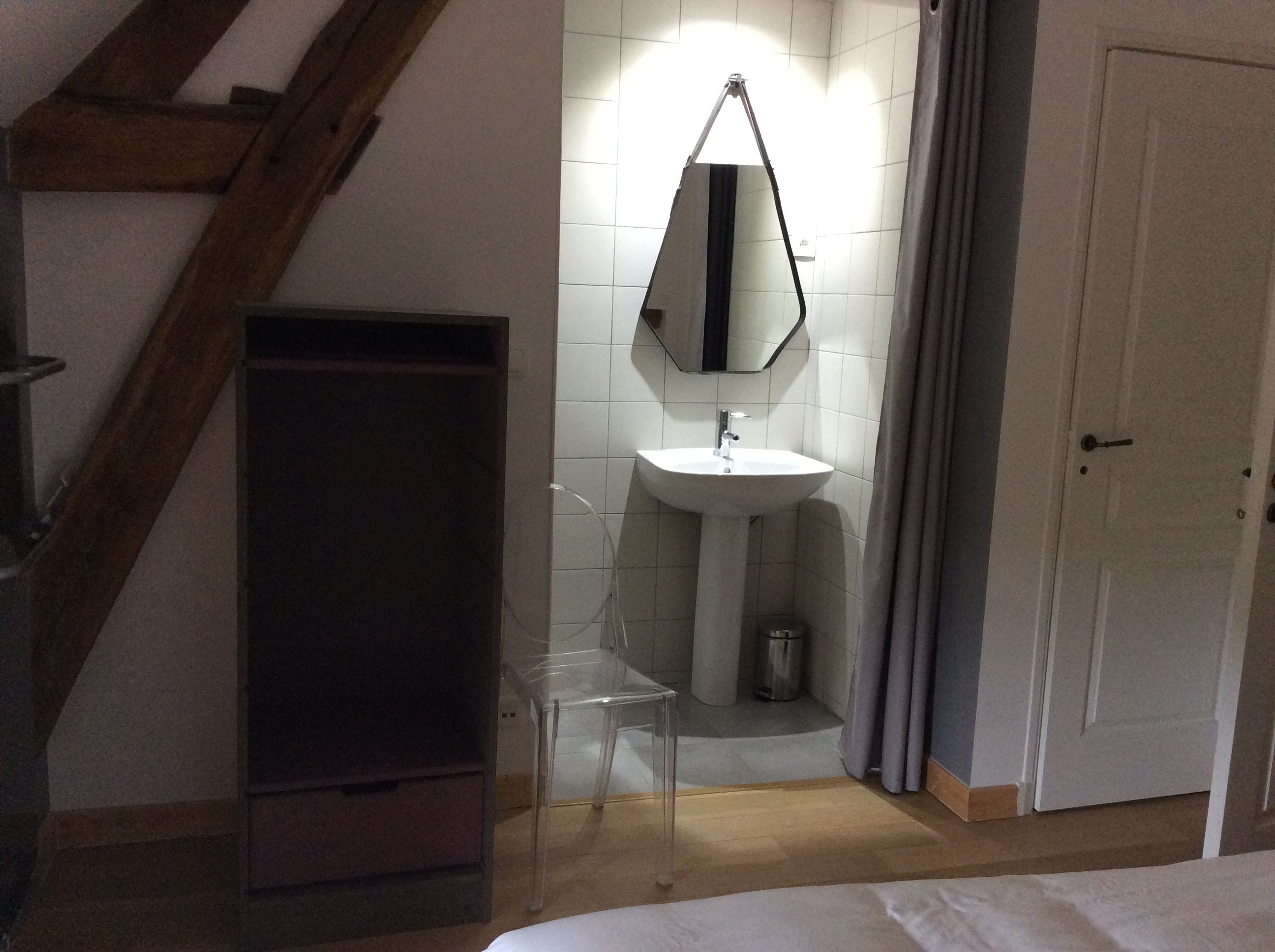 A bedroom with a wooden staircase, a white sink with a mirror, a clear plastic chair, and a closed door.