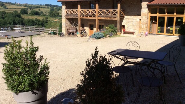 A rustic building with a stone facade, wooden balcony, and outdoor seating area with tables and chairs. - Domaine de Noyer (Saint-Christophe-en-Brionnais)