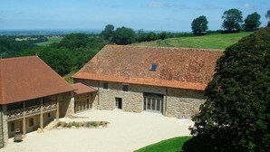 A stone building with a tiled roof, a covered porch, and a view of the surrounding countryside. - Domaine de Noyer (Saint-Christophe-en-Brionnais)
