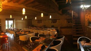 A restaurant with multiple dining tables and chairs, wooden beams on the ceiling, and hanging pendant lights. - Domaine de Noyer (Saint-Christophe-en-Brionnais)