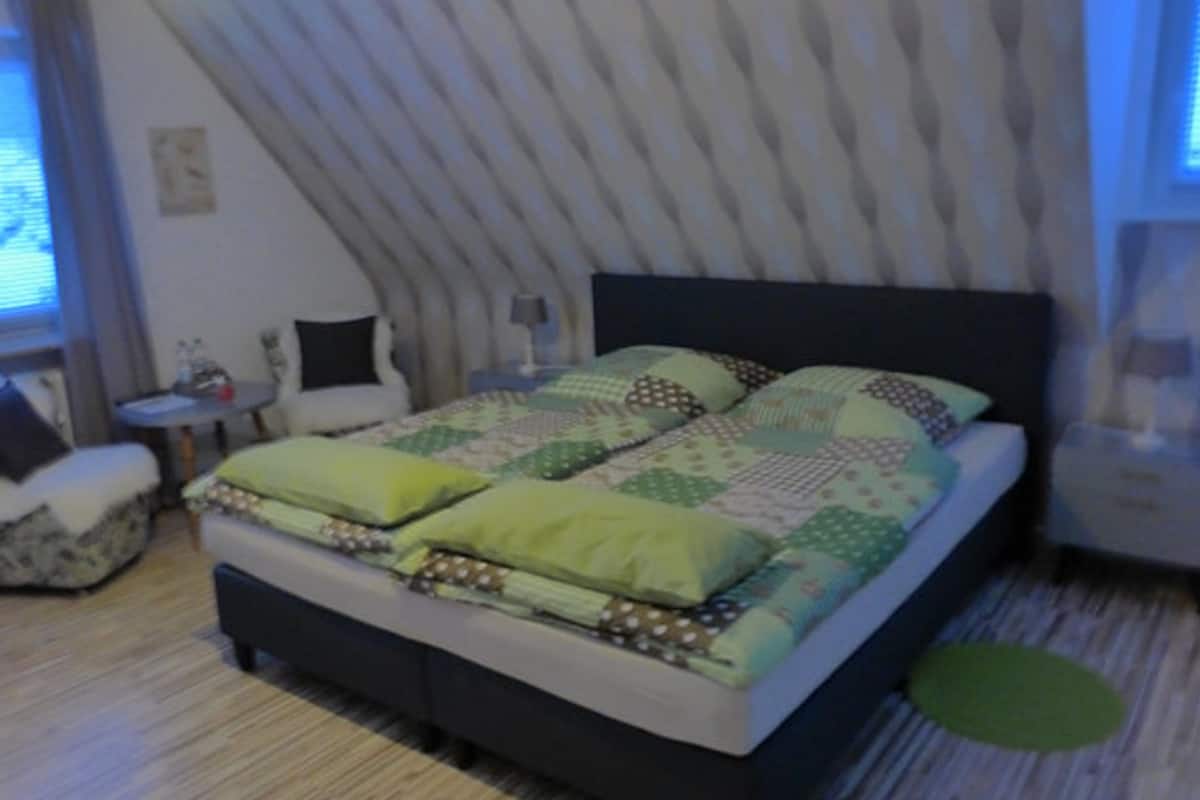 Une chambre à coucher avec un lit, une petite table, une chaise et une fenêtre avec des rideaux.