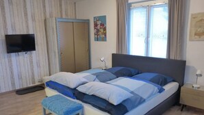 A bedroom with a bed, a bench, a TV, a wardrobe, and a window with curtains.