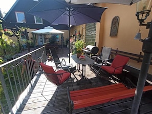Een terras buiten met een tafel en stoelen, een barbecue en een pergola met parasols.