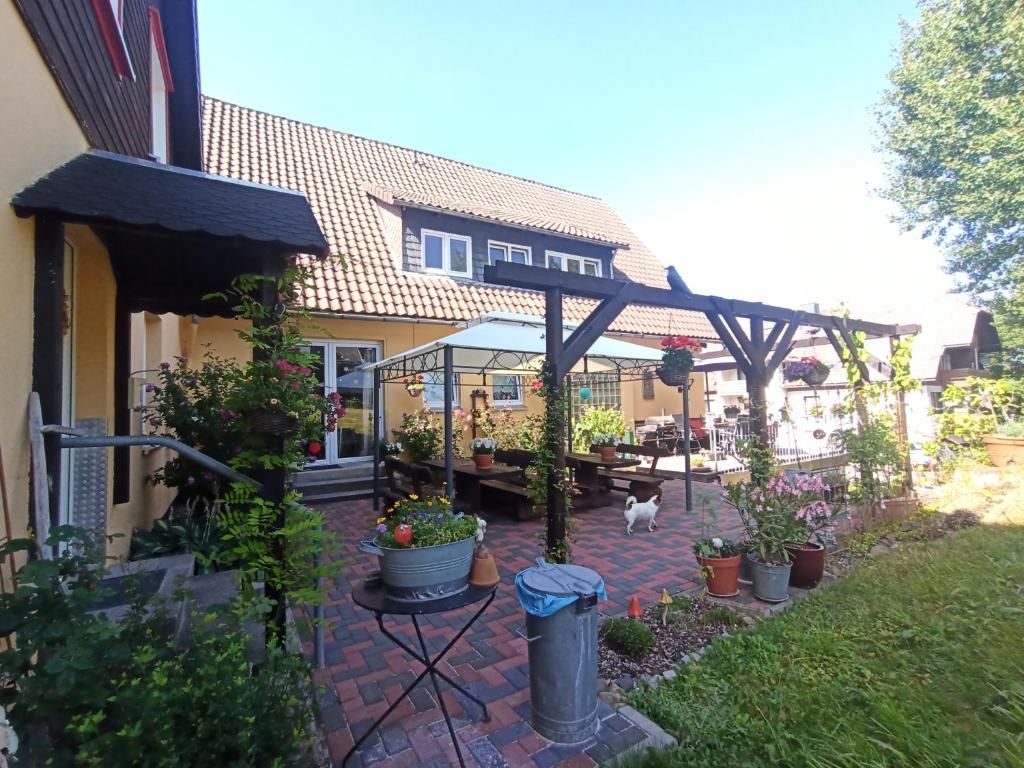 Ein Haus mit Ziegeldach, einer überdachten Terrasse mit Blumentöpfen und einem kleinen Hund.