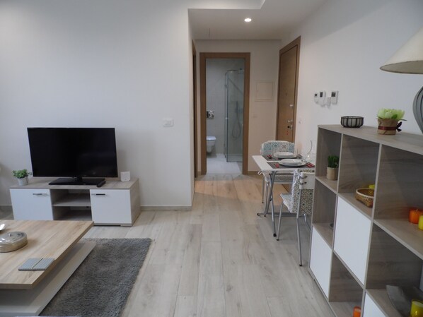 A modern living room with a flat-screen TV, a coffee table, and a dining area with a table and chairs.