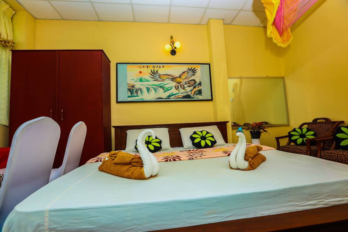A hotel room with a bed, a wardrobe, a painting, and a chandelier.