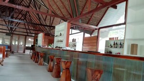 A spacious bar area with a high ceiling and wooden beams, featuring a long counter with stools and shelves stocked with bottles.