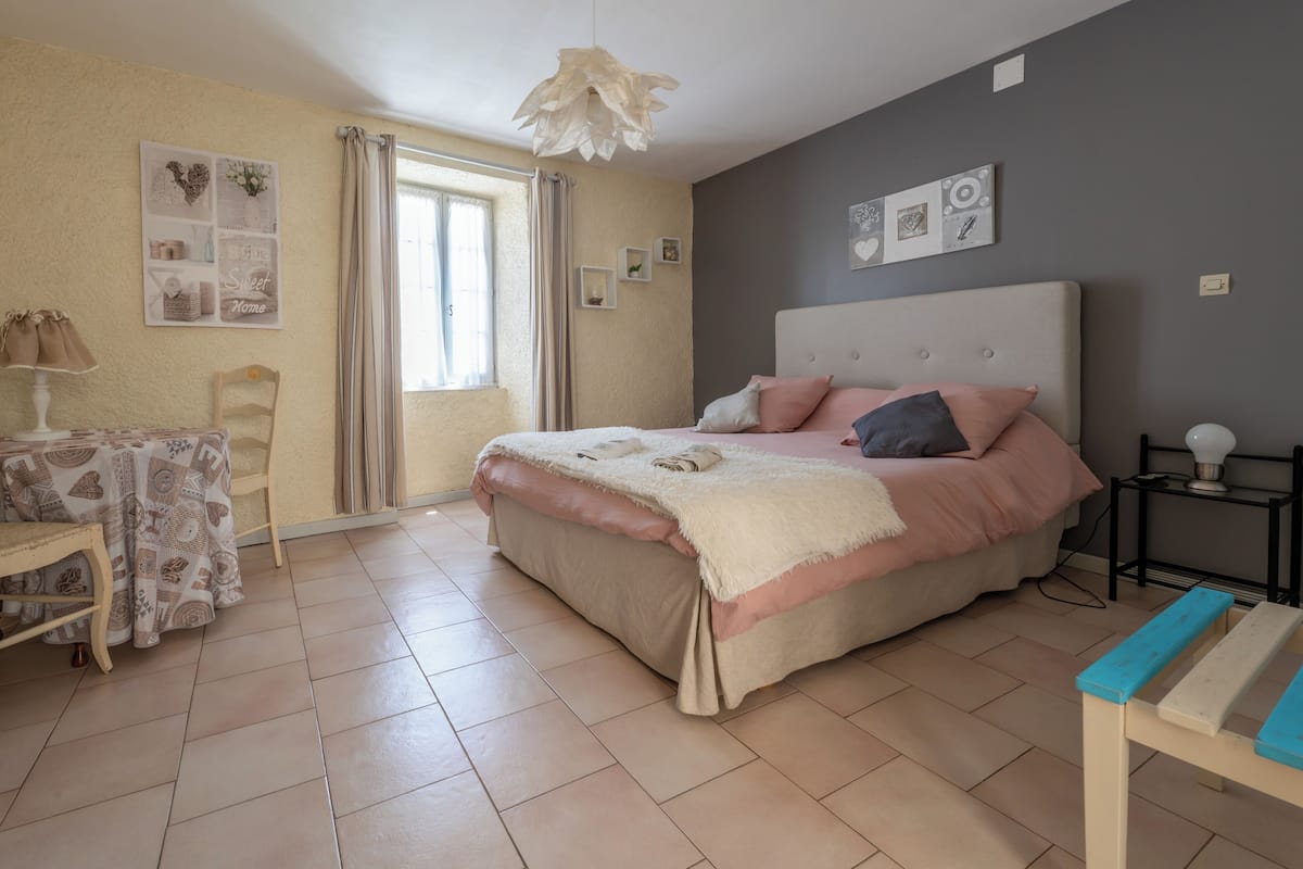Une chambre à coucher avec un lit, une table de chevet, une chaise et une fenêtre avec des rideaux.
