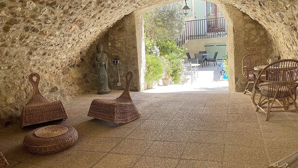 Un intérieur aux murs de pierre, agrémenté d’une statue, de meubles en osier et offrant une vue sur un balcon extérieur.