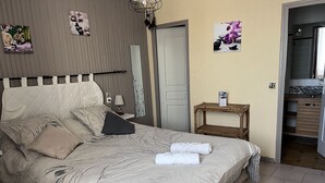 Un lit bien fait, recouvert d’une couvre-lit à motifs, une table de chevet avec une lampe et une petite étagère avec un livre.