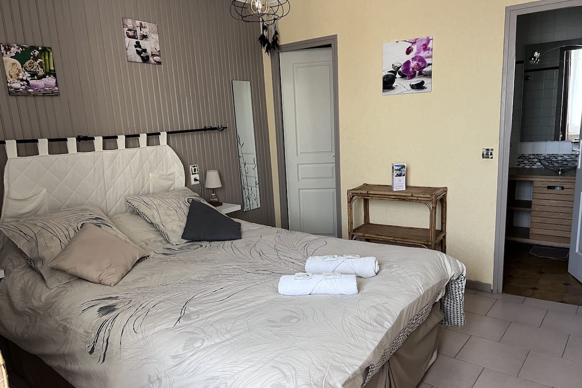 Un lit bien fait, recouvert d’une couvre-lit à motifs, une table de chevet avec une lampe et une petite étagère avec un livre.