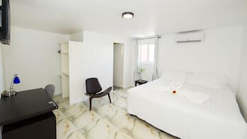 A hotel room with a bed, a desk, a chair, a TV, and an air conditioning unit.