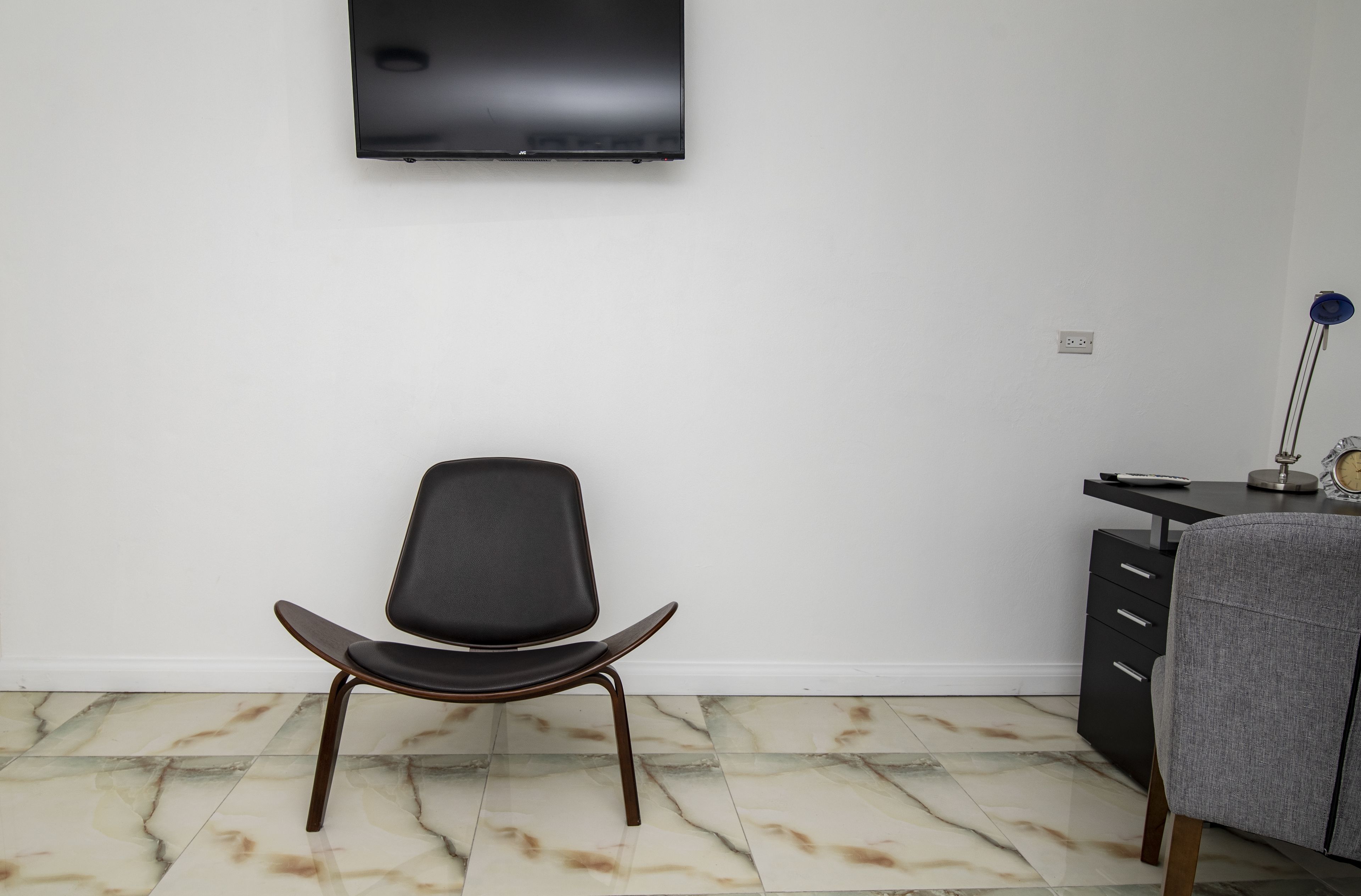 Una habitación moderna con una silla negra, un escritorio con lámpara y un televisor montado en la pared.