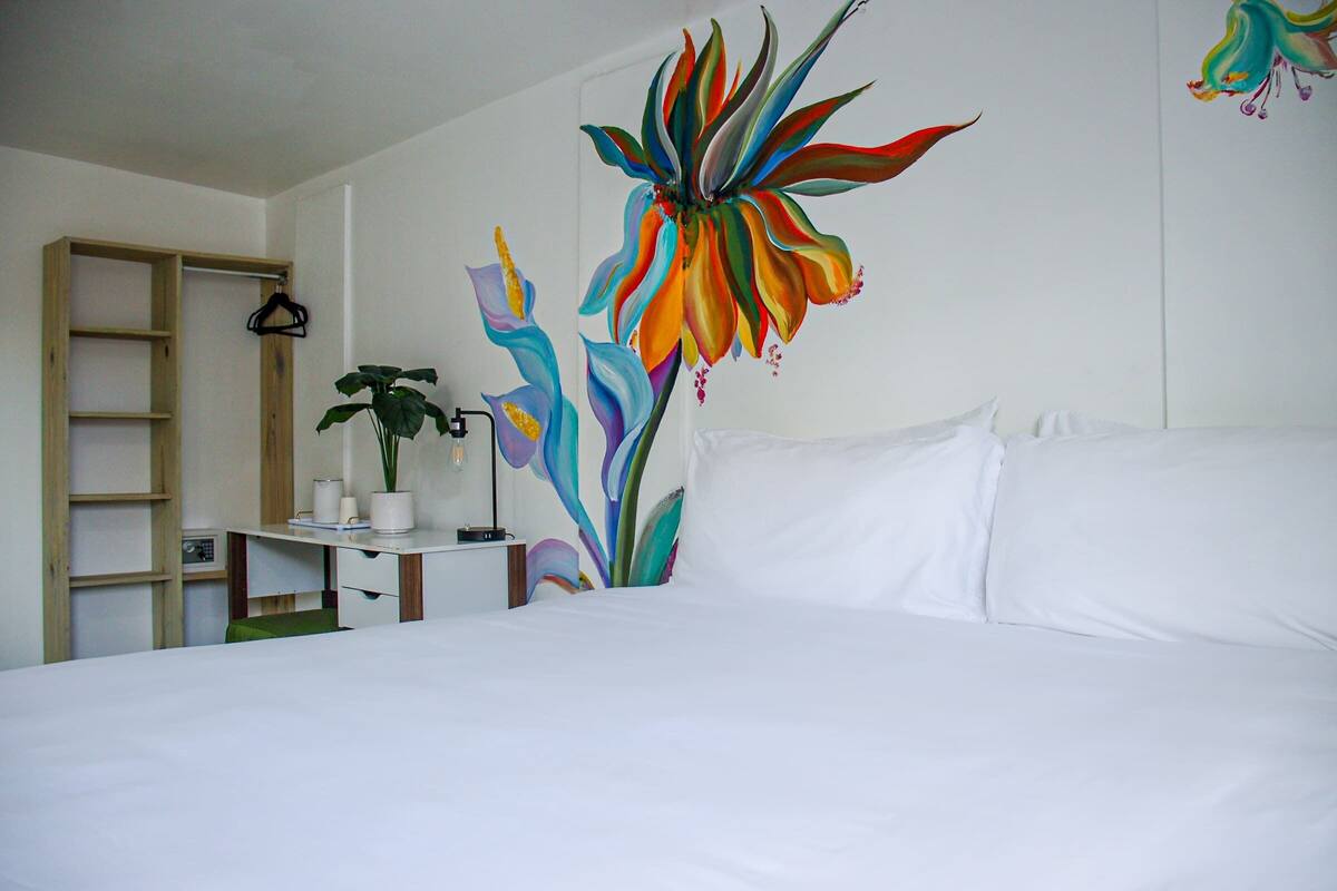 A bedroom with a bed, a shelf with a plant, and a colorful wall mural.
