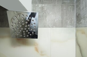 Un baño moderno con un cabezal de ducha cuadrado montado en una pared de mármol blanco.