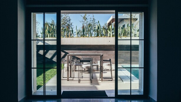 Ein modernes Interieur mit einem großen Fenster, das einen Innenhof mit Gartenmöbeln und einem Pool zeigt.
