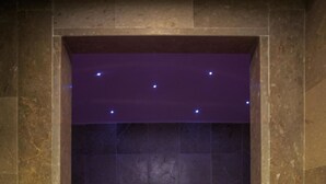 Ein Badezimmer mit Steinwänden, einer Marmortonne, violetter Beleuchtung und modernem Design.