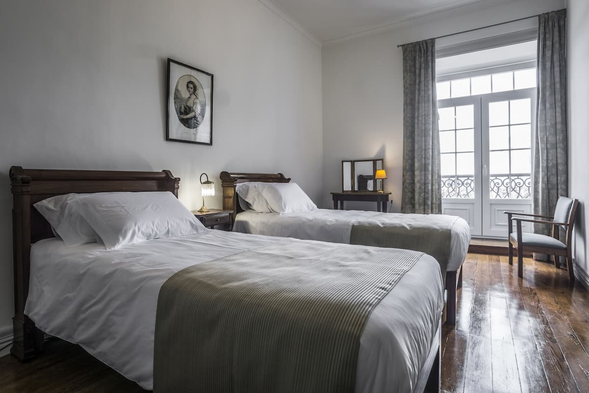 Een hotelkamer met twee bedden, een nachtkastje met lamp, een stoel en een raam met gordijnen.