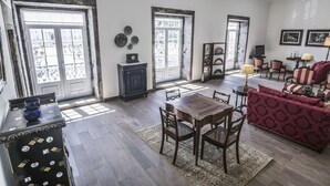 Ein geräumiges Wohnzimmer mit einem Holzessttisch, zwei Stühlen, einem rot gemusterten Sofa und einem Fernseher.