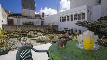 A patio with a table set for two, surrounded by potted plants and a garden.