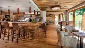 A spacious bar area with wooden bar stools and a counter, surrounded by large windows offering a view of the outdoors. - Aktivhotel Gasteiner Einkehr (Dorfgastein)