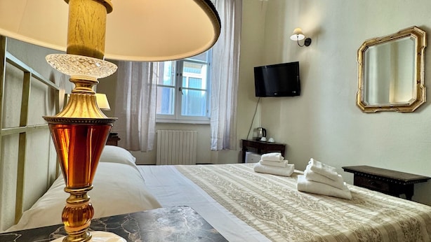 A hotel room with a bed, a TV, a mirror, and a lamp. - Lucca Charm (Lucca)