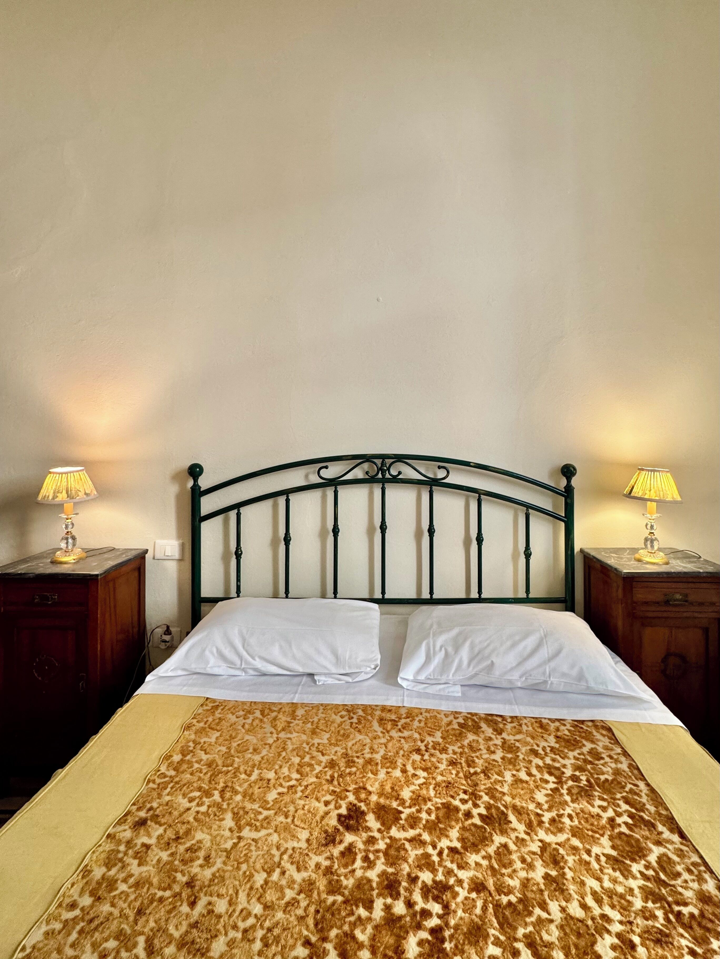 A bed with a patterned bedspread, two bedside lamps, and a metal headboard.