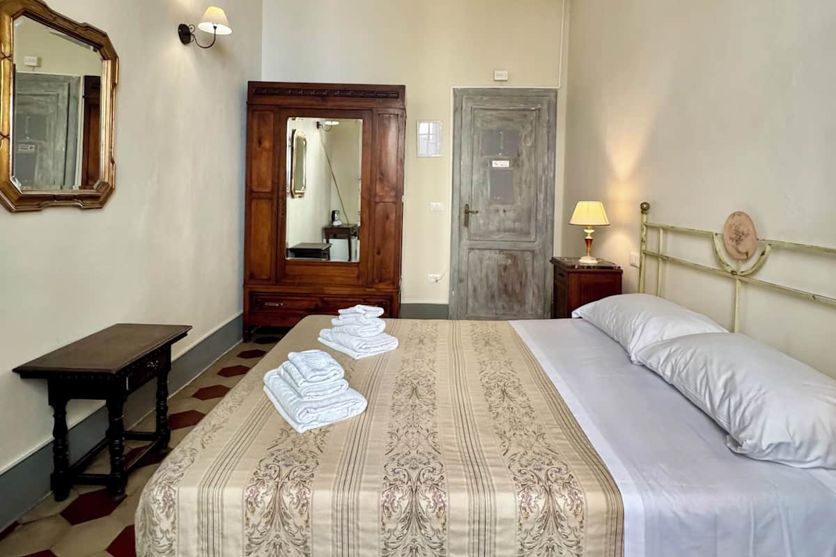 A hotel room with a large bed, a wooden wardrobe, a small table, and a mirror on the wall.