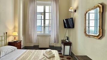 Habitación de hotel con una cama grande, televisión, espejo, una mesita y ventana con cortinas.