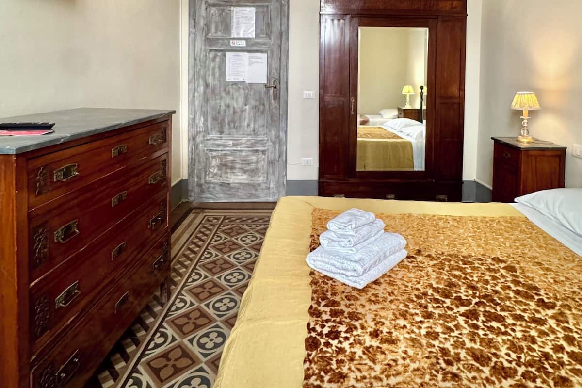 A bedroom with a bed, a wooden dresser, a television, an air conditioning unit, and a patterned floor.