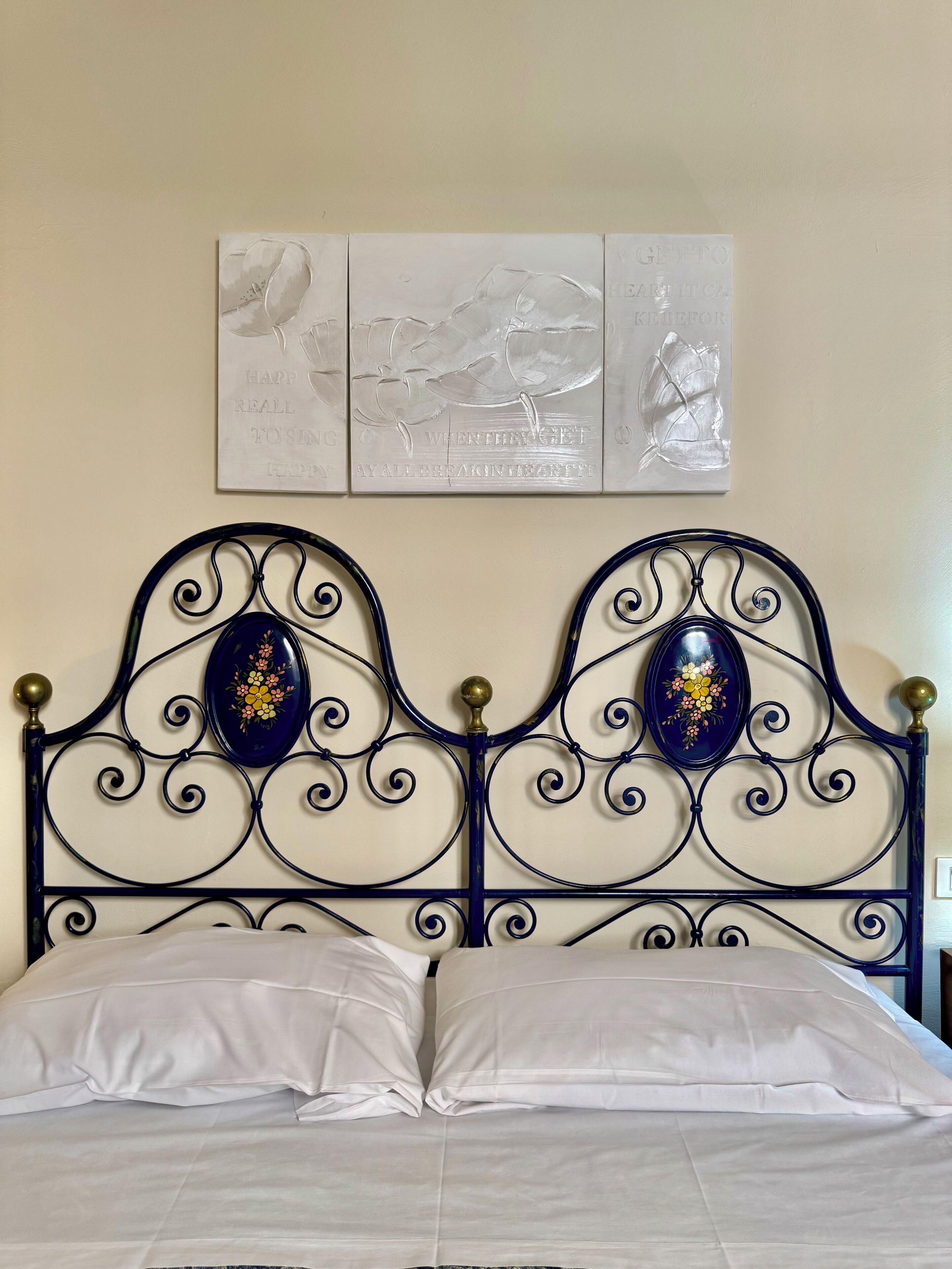 A bed with a metal headboard, two decorative oval-shaped panels, and a wall-mounted artwork above.