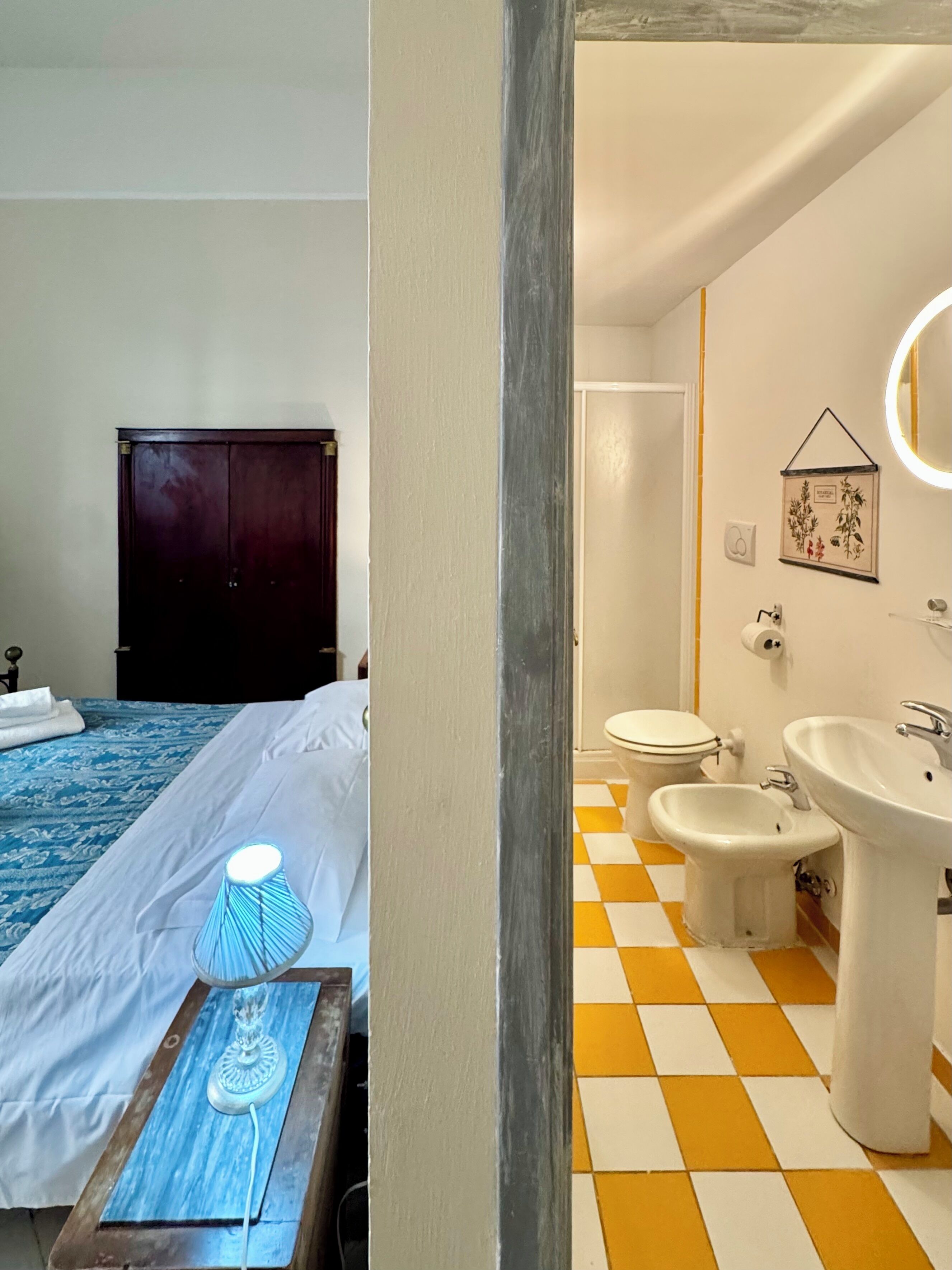 A hotel room with a bed, bedside lamp, and a bathroom with a toilet, bidet, and sink.