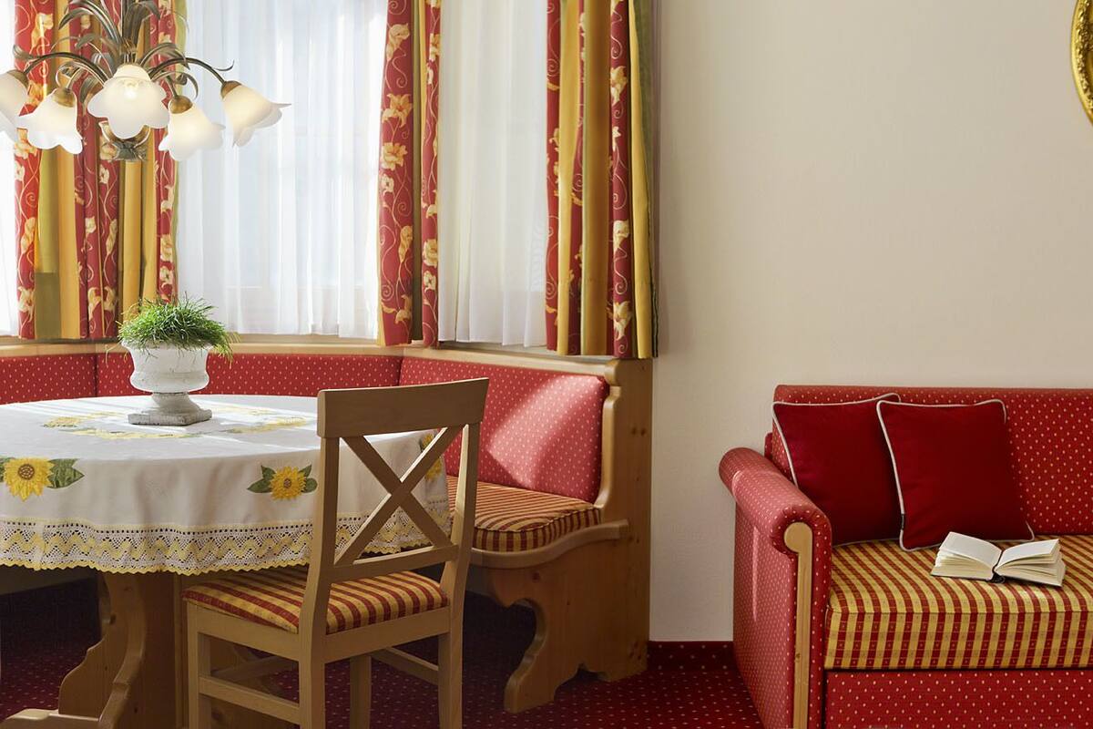 Ein gemütliches Zimmer mit Esstisch, einem Holzstuhl, einem roten Sofa und einem Fenster mit Vorhängen.